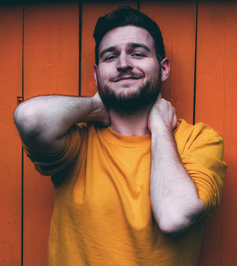 Scottish Actor, dancer, director, Andi Denny photographed in Glasgow's West End. He is pictured against a yellow wooden door, wearing a similarly coloured yellow jumper.