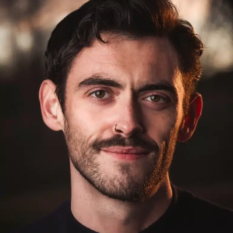 Headshot of Calvin, photographed in the golden hour on the streets of Glasgow. He is lit by the warm sunset light and looks directly to camera.