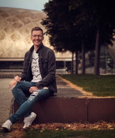 Jon, photographed at Pacific Quay in Glasgow close to sunset on a summer's evening, The sunlight can be seen against Glasgow Science Centre in the background.